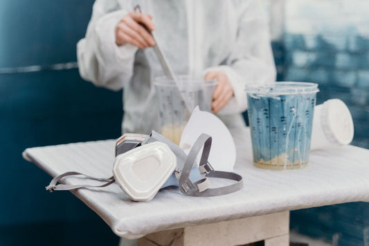 An artist in protective gear mixes blue paint with safety equipment in a workshop.